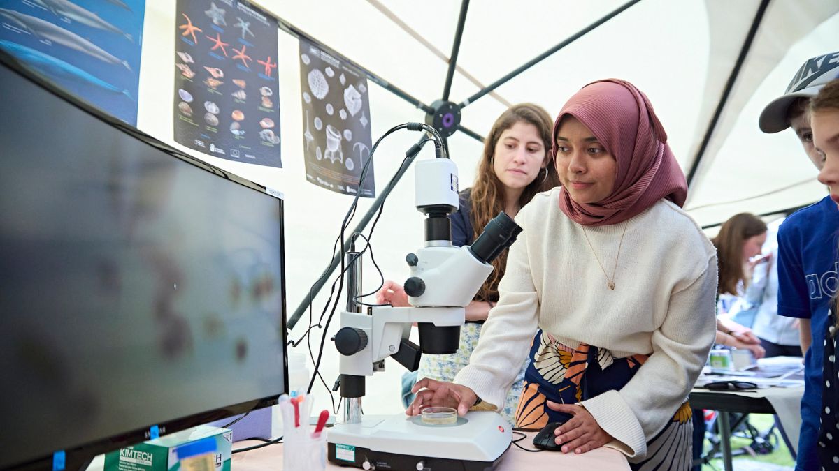 Woman looking at screen with microscope and showing others