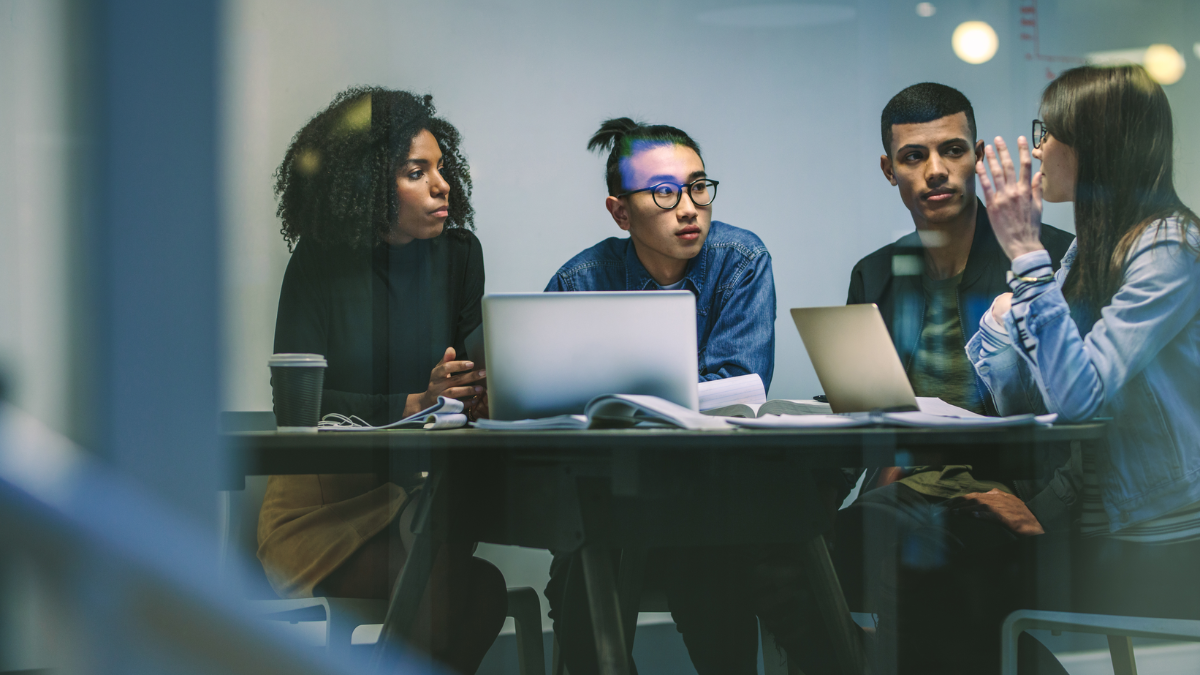 Group of people sitting round a table with laptops talking
