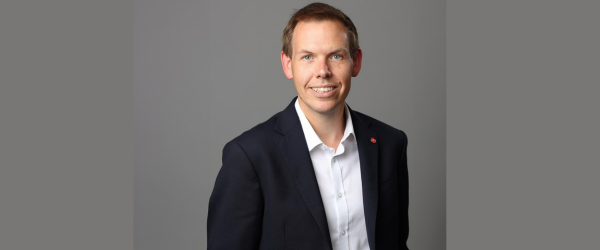 Portrait photo of Professor Paul Shearing. He stands against a grey background wearing a black jacket and white shirt.