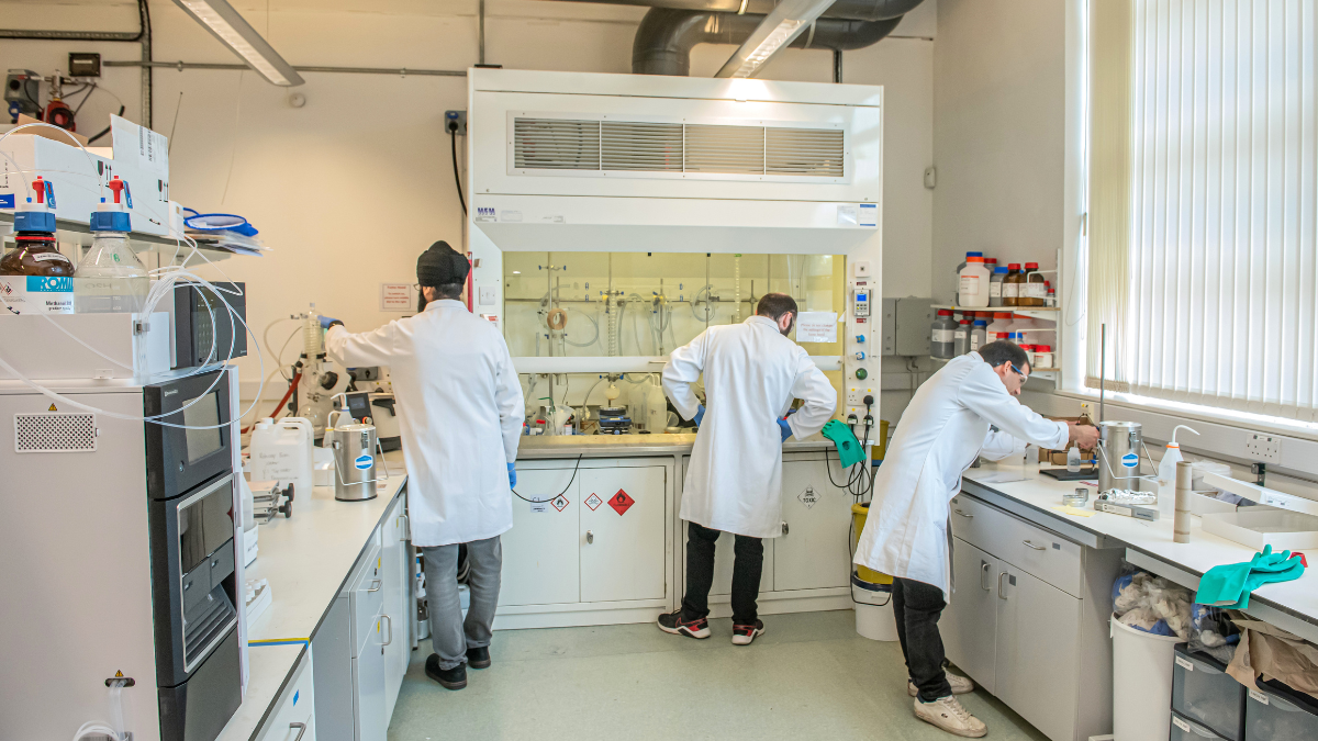 Three people standing in a lab with their backs to the camera working at benches