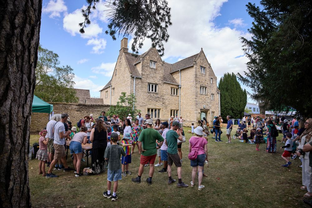People mingling outside at a garden party with a large farmhouse in the background