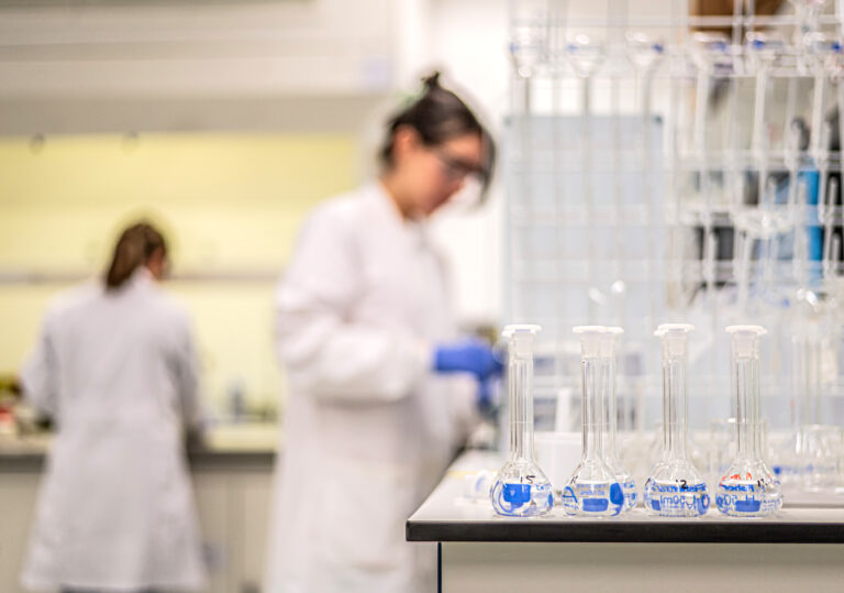 A row of test tubes in a laboratory with scientists working in the background