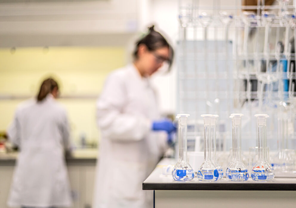 A row of test tubes in a laboratory with scientists working in the background