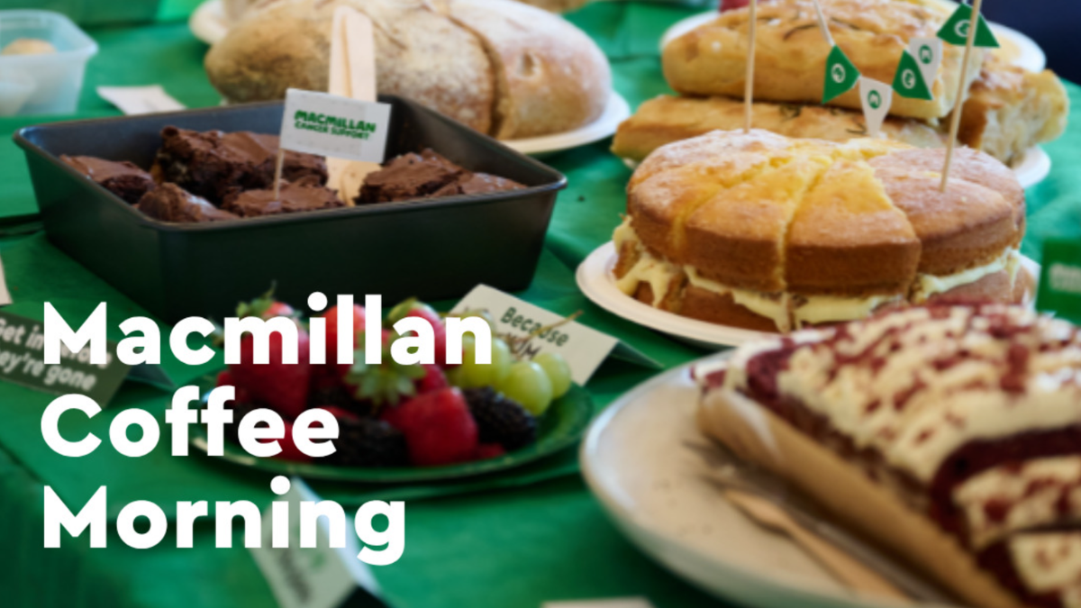 A table with a green tablecloth and a selection of cakes and the wording: Macmillan Coffee Morning